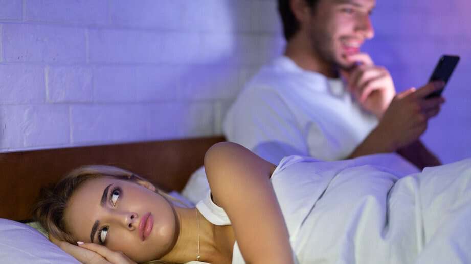 man texting in bed while woman sleeps