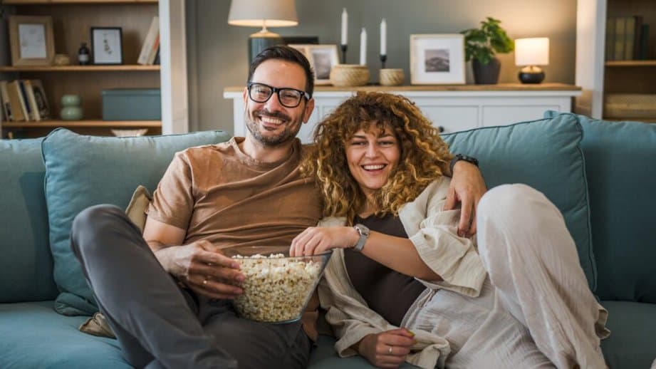man and woman eating popcorn on a couch watching TV