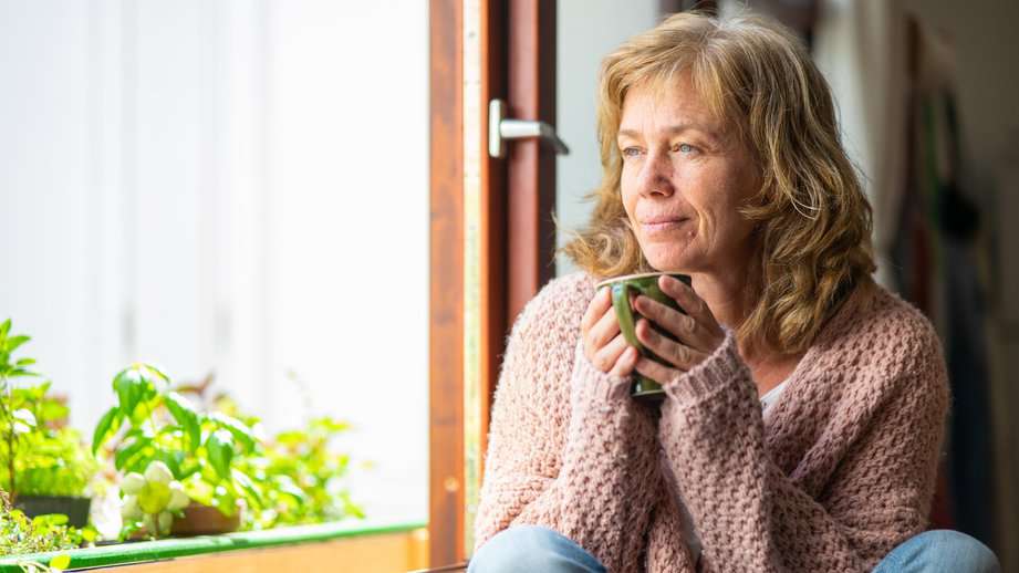 woman looking out window with coffee cup