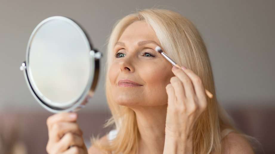 older woman doing her makeup in the mirror